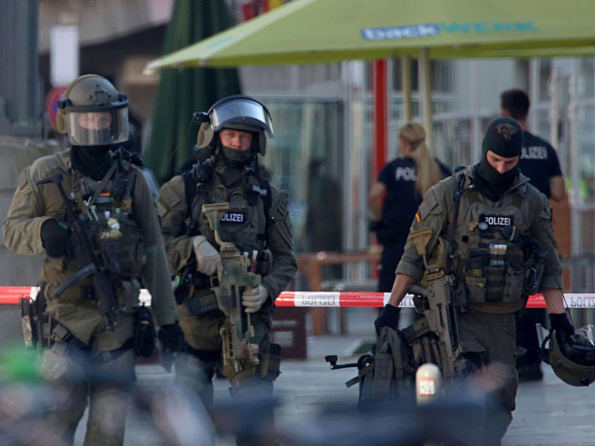 Vermummte und schwer bewaffnete Spezialkräfte sind vor einer Polizeiabsperrung im Einsatz.