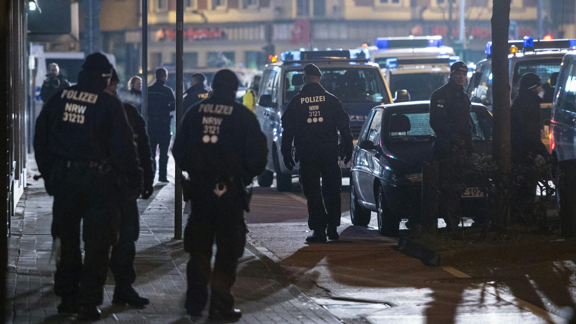 Mehrere Polizeifahrzeuge stehen auf einer Straße – Polizistinnen und Polizisten kontrollieren Personen.