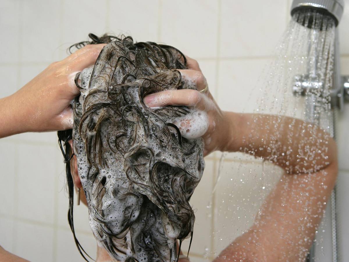 Eine Frau steht unter der Dusche und wäscht sich die Haare.