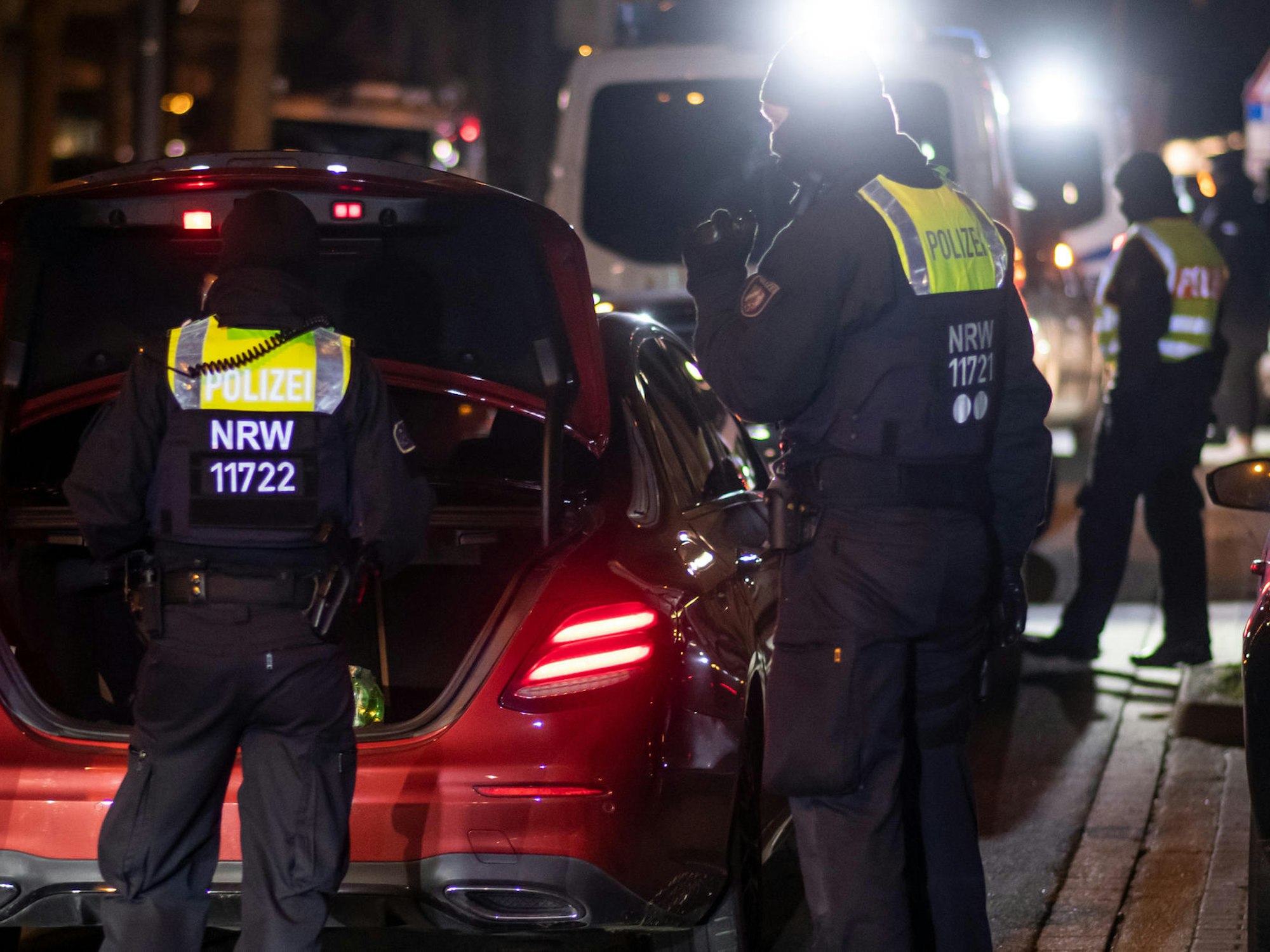 Einsatzkräfte der Polizei stehen an einem Auto und gucken in den Kofferraum.