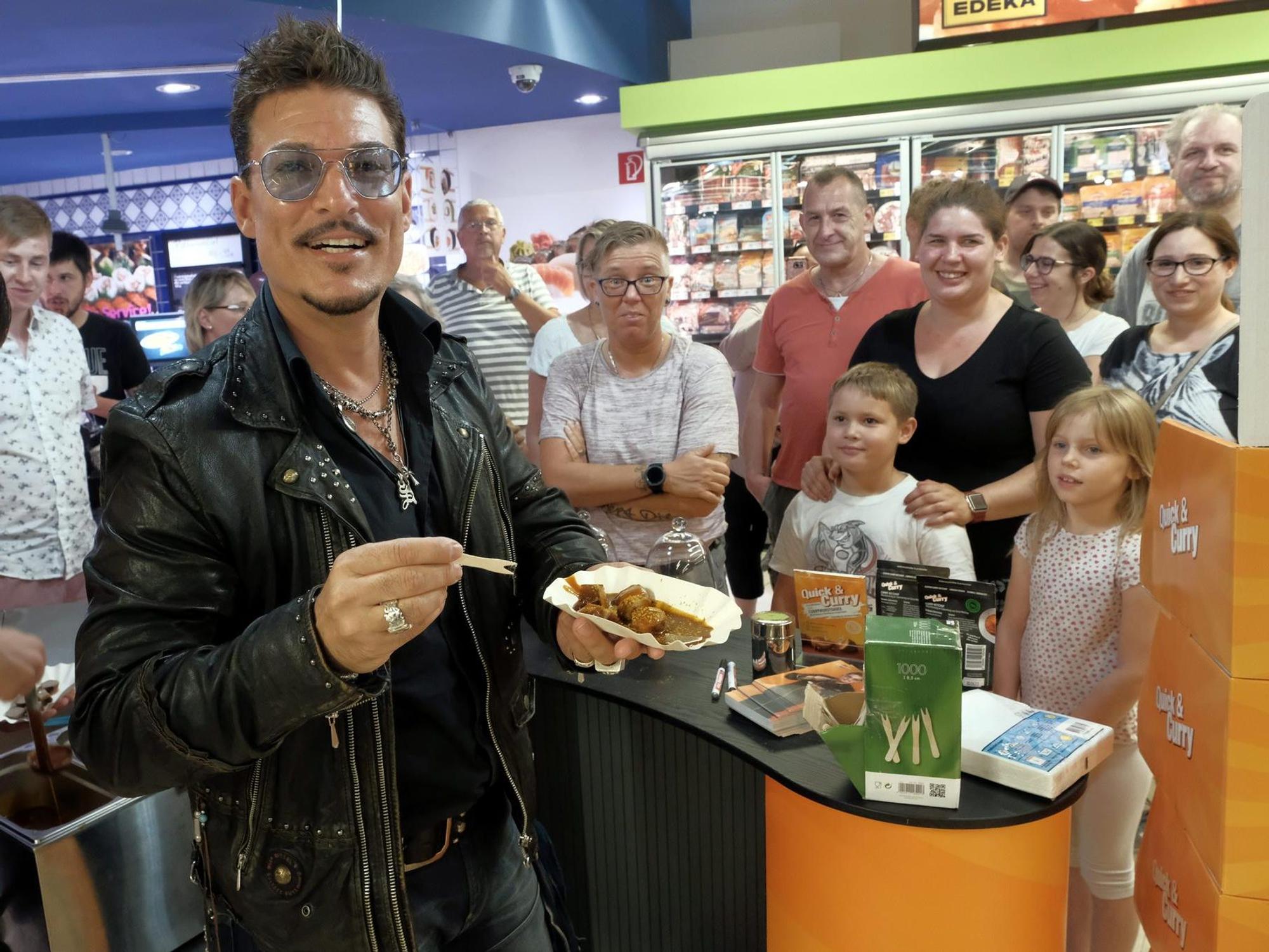 Chris Töpperwien verteilt Currywurst in einem Kölner Supermarkt.