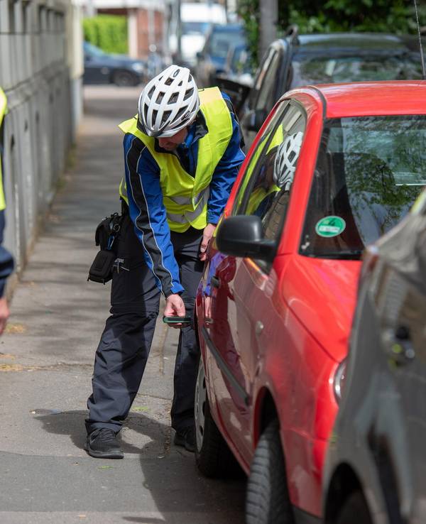 Eine Person hält ein Gerät an ein Auto, um den Abstand zum Haus zu messen.