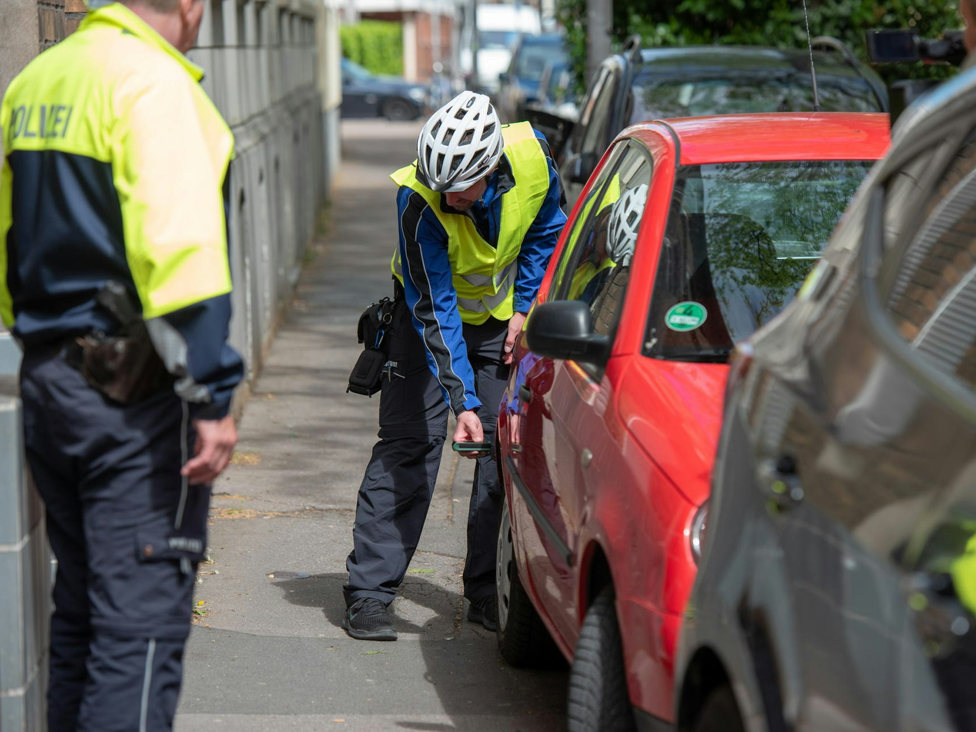 Eine Person hält ein Gerät an ein Auto, um den Abstand zum Haus zu messen.