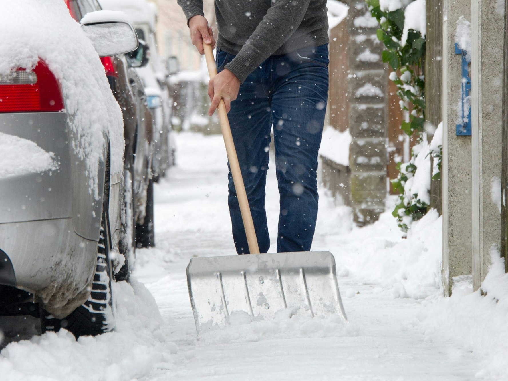 Ein Mann befreit den Gehweg mit einer Schippe von Schnee,