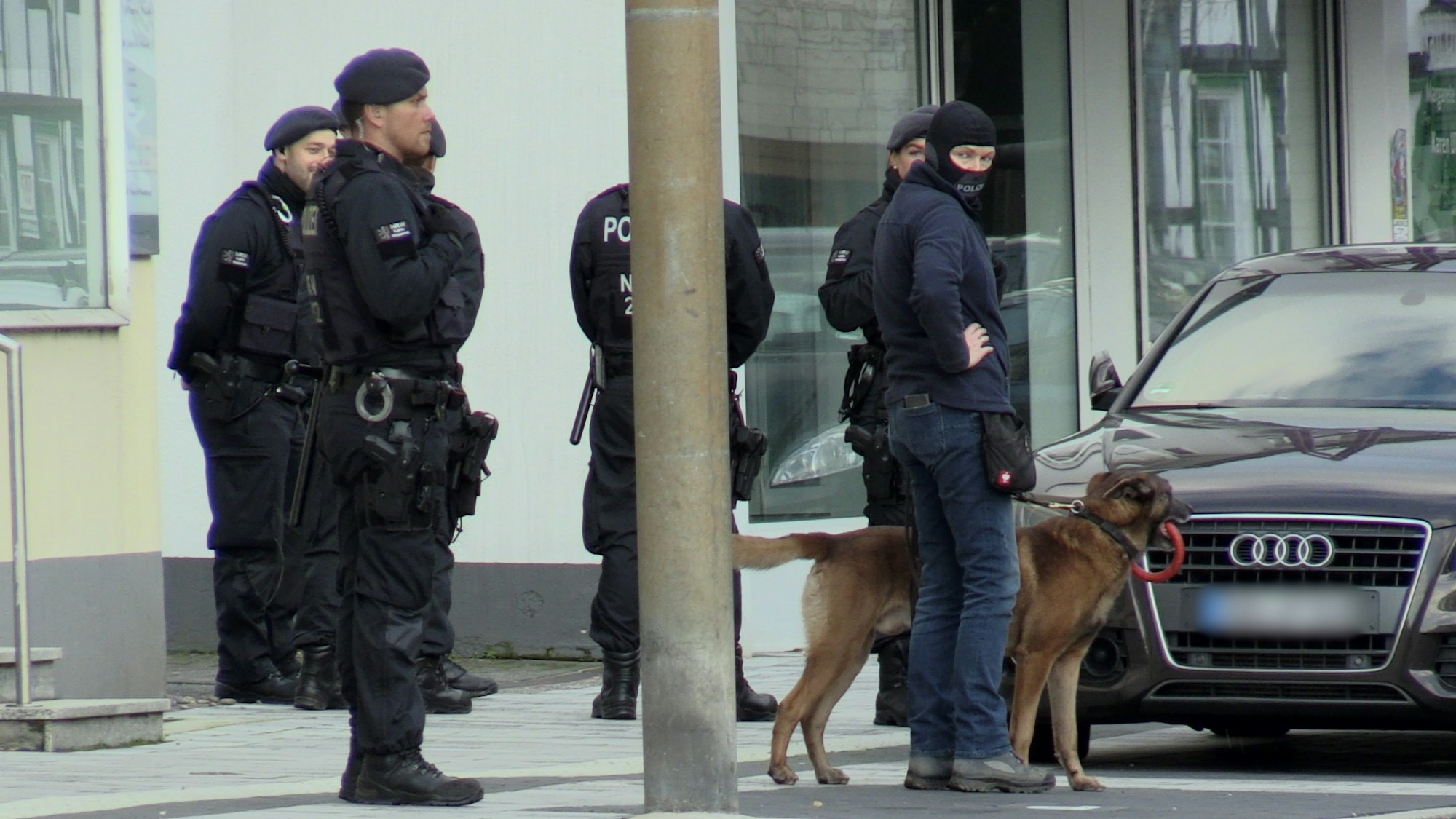 Zum Teil vermummte Einsatzkräfte stehen vor einem Haus.