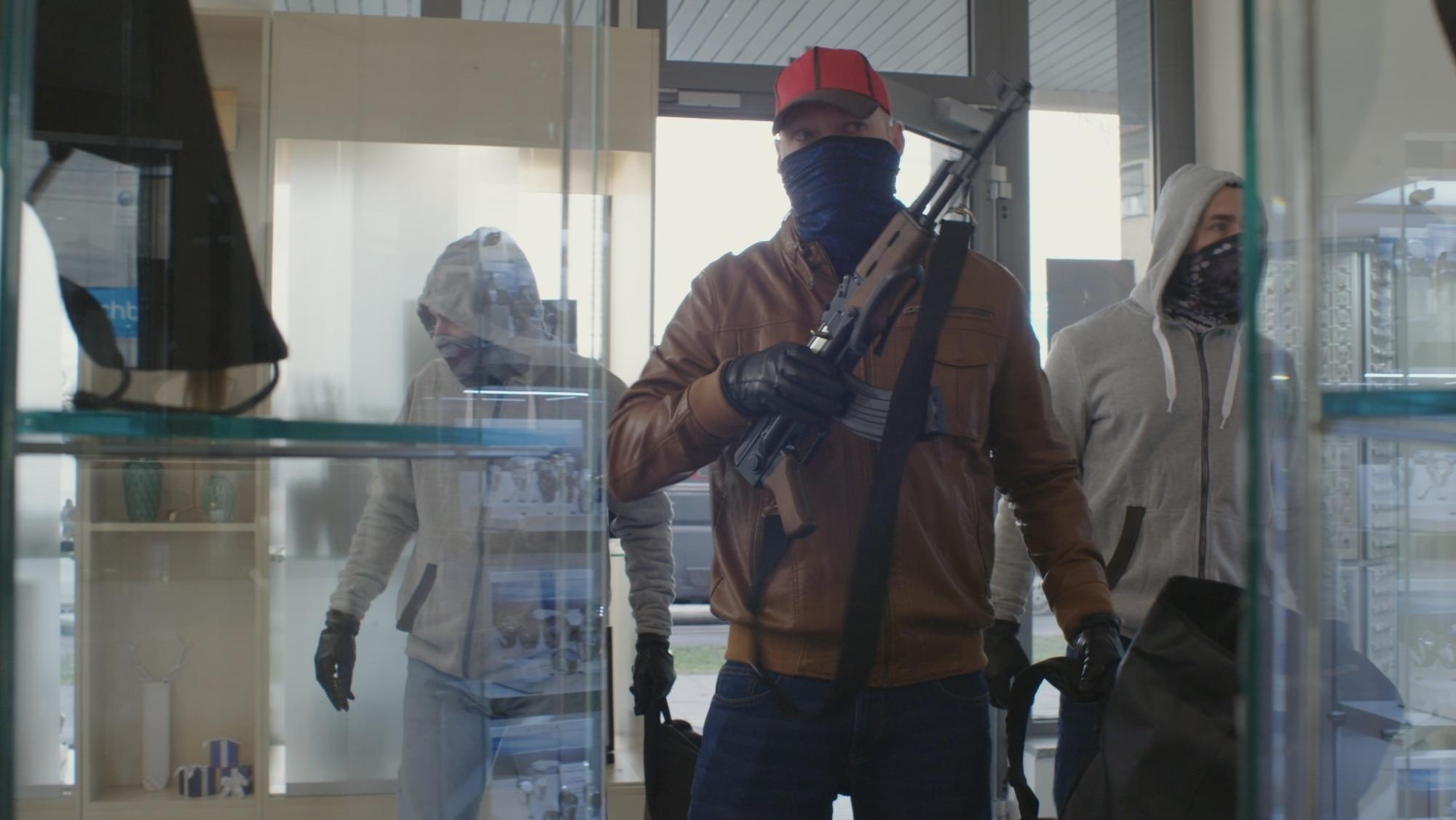 Drei vermummte Männer betreten ein Juweliergeschäft, einer ist mit einem Sturmgewehr bewaffnet.