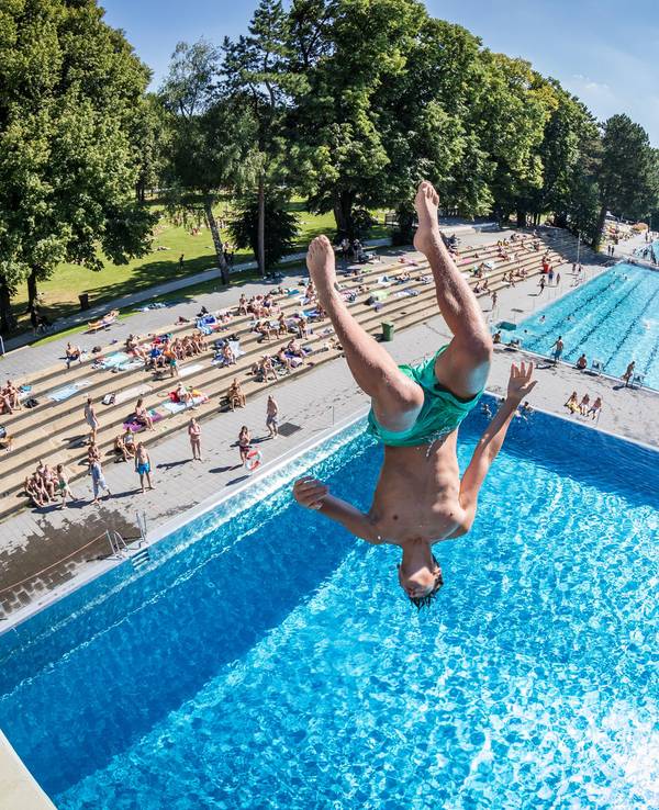 Ein junger Mann stürzt sich kopfüber von einem Sprungturm ins Schwimmbecken.