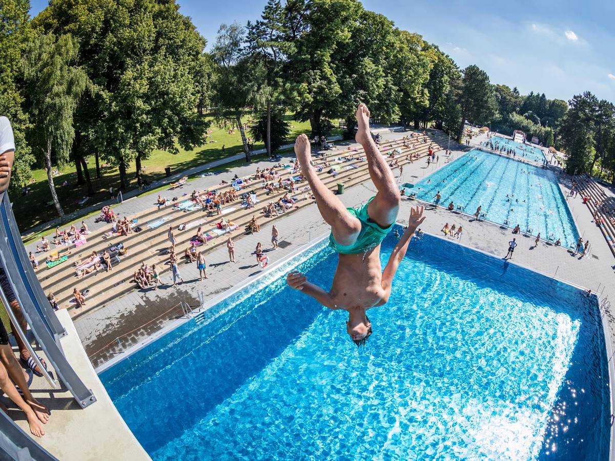 Ein junger Mann stürzt sich kopfüber von einem Sprungturm ins Schwimmbecken.