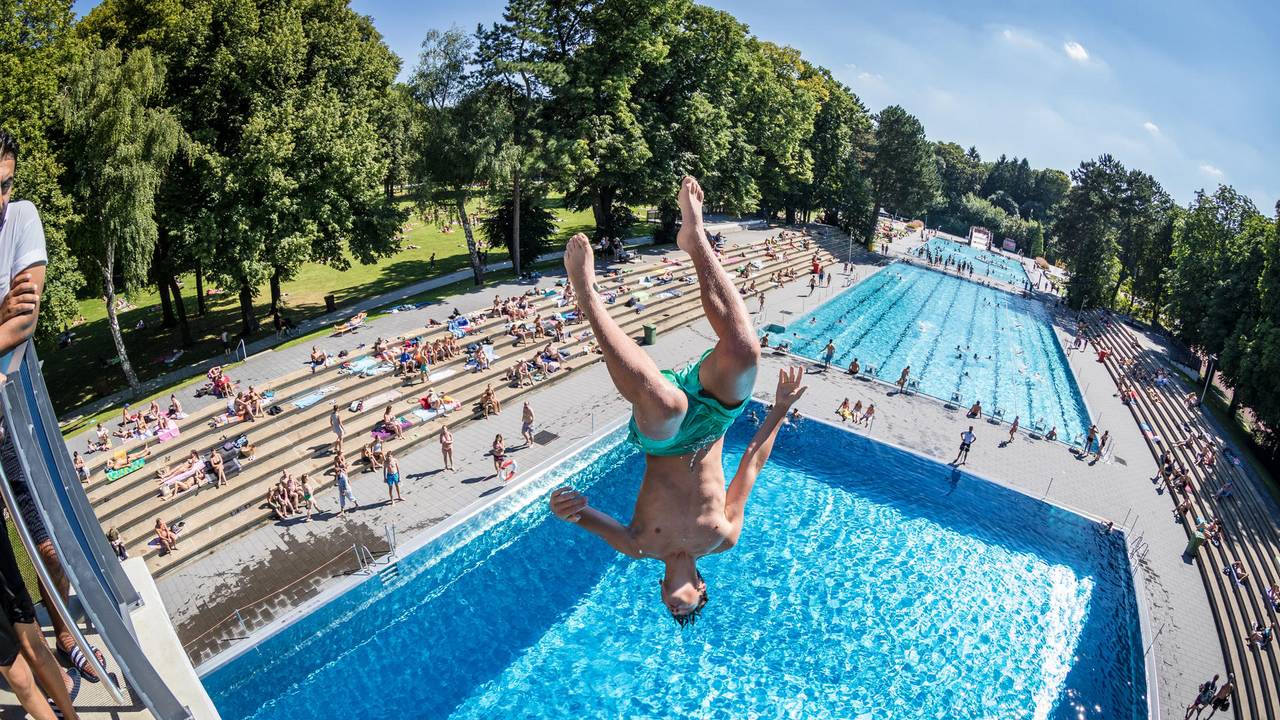Ein junger Mann stürzt sich kopfüber von einem Sprungturm ins Schwimmbecken.