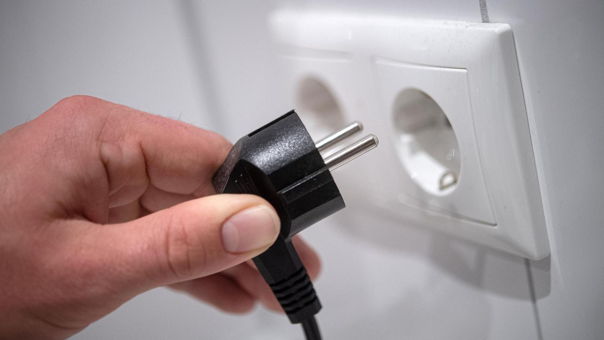 Eine Person will einen Stecker in die Steckdose stecken. In einigen Kölner Stadtteilen war das Mittwochnachmittag vergeblich, dort war der Strom weg.