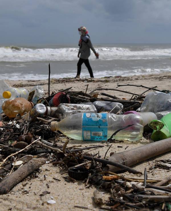 Frau geht am Strand spazieren, im Vordergrund liegen Plastikflaschen.