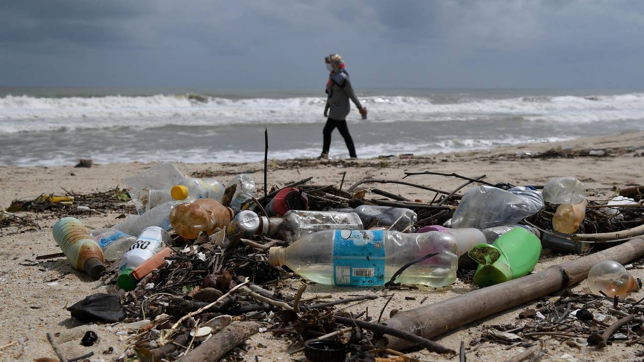 Frau geht am Strand spazieren, im Vordergrund liegen Plastikflaschen.
