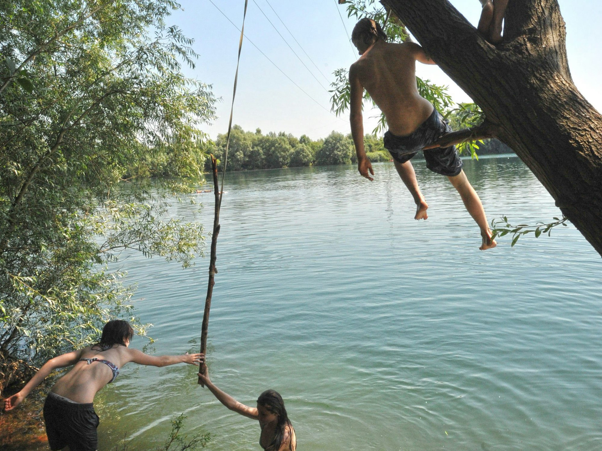 Junge Menschen klettern am Ufer eines Badesees