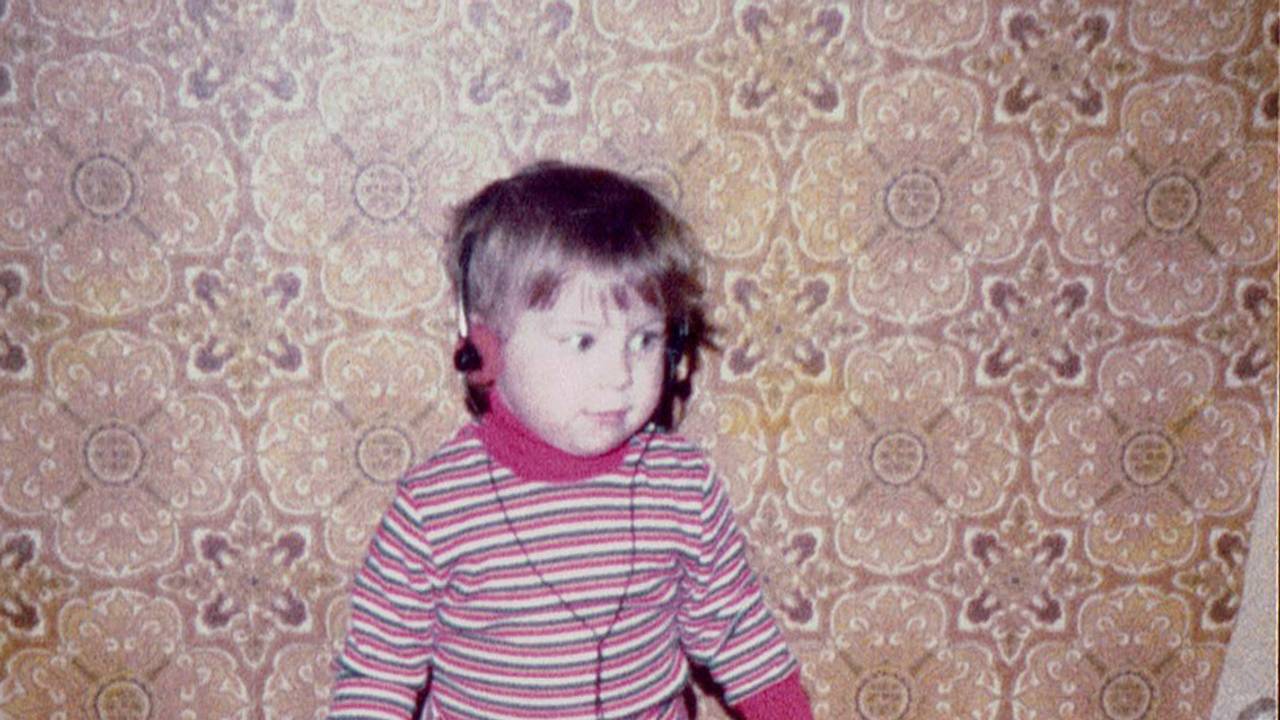 Kerstin Ott als Kind im bunt gestreiften Pullover, mit einem Kopfhörer auf der wuscheligen Frisur, der zugehörige Walkman baumelt an den Beinen.