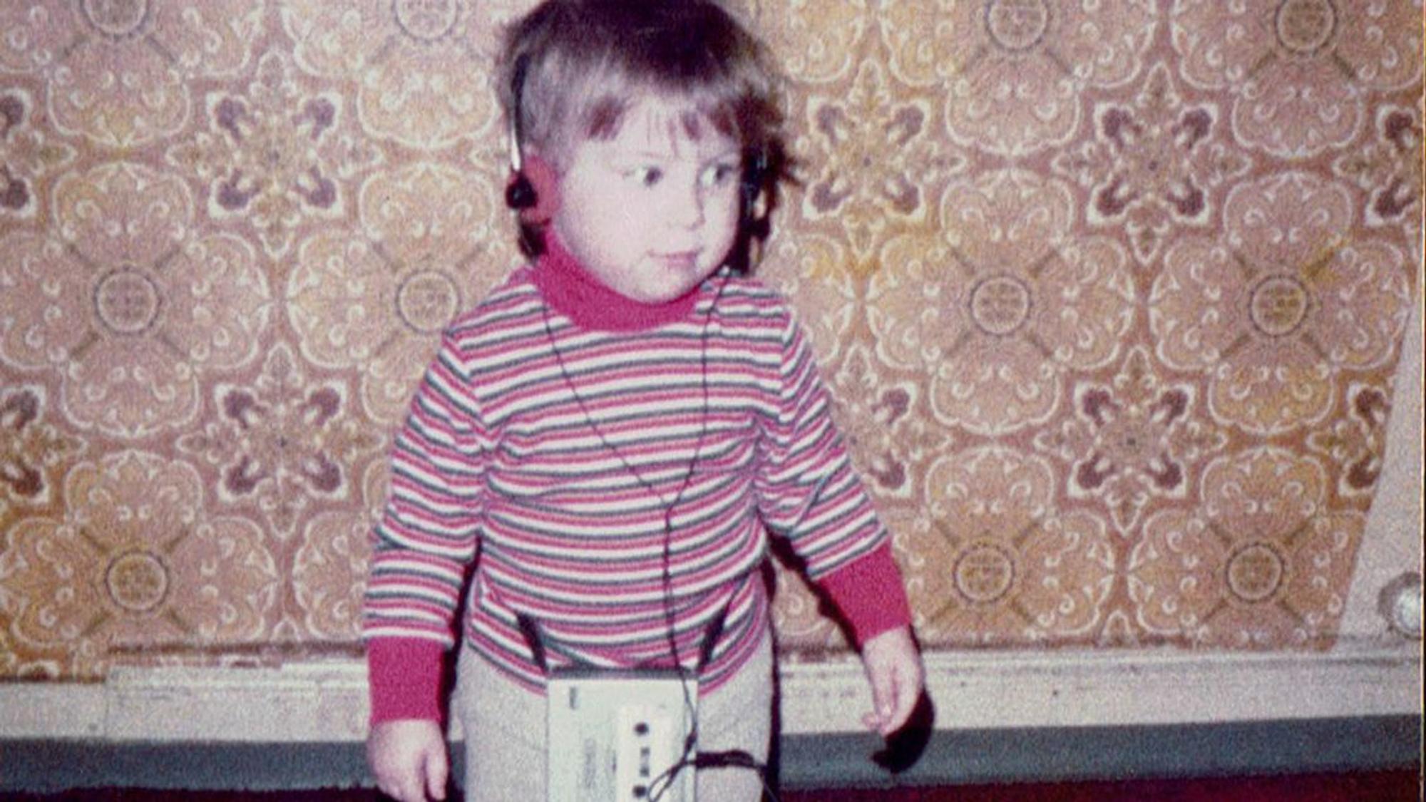 Kerstin Ott als Kind im bunt gestreiften Pullover, mit einem Kopfhörer auf der wuscheligen Frisur, der zugehörige Walkman baumelt an den Beinen.
