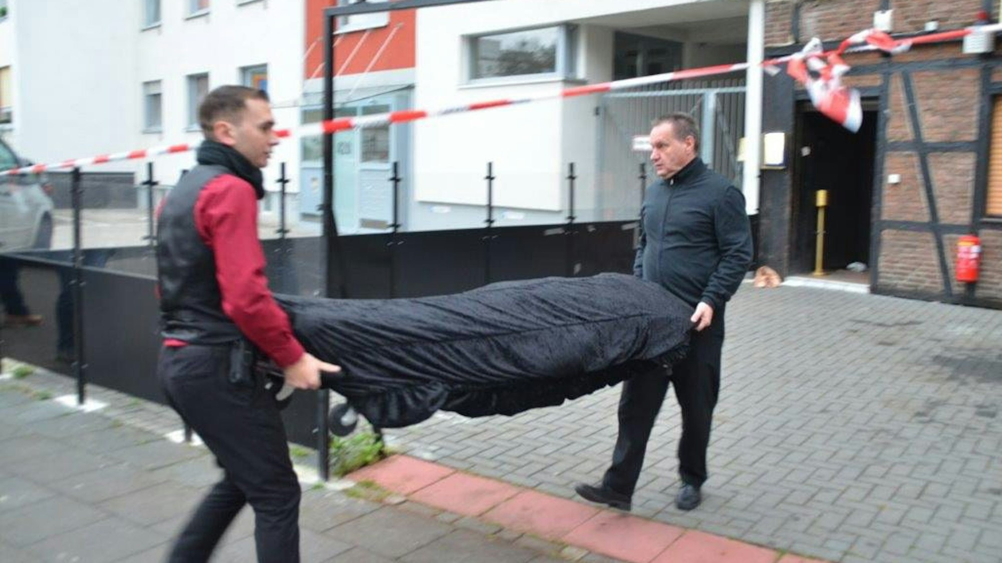 Zwei Bestatter tragen eine Leiche weg.