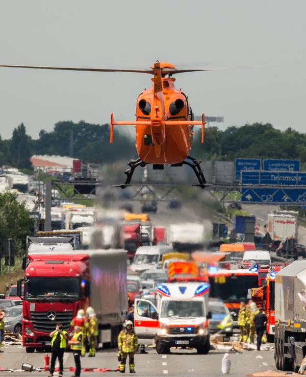 Ein Rettungshubschrauber fliegt zu einer Unfallstelle auf einer Autobahn. Dort stehen zwei beschädigte Lkw, daneben steht ein Rettungswagen, zahlreiche Einsatzkräfte befinden sich auf der Fahrbahn.