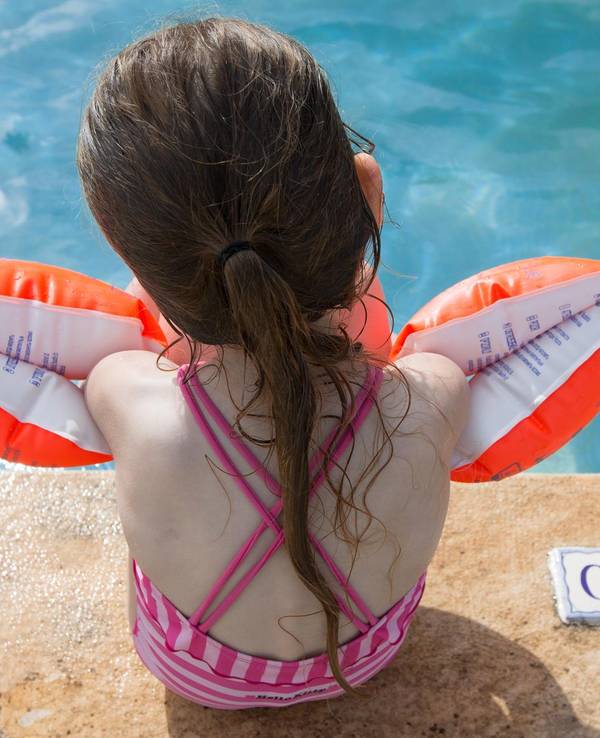 Ein Mädchen sitzt mit Schwimmflügeln am Beckenrand.