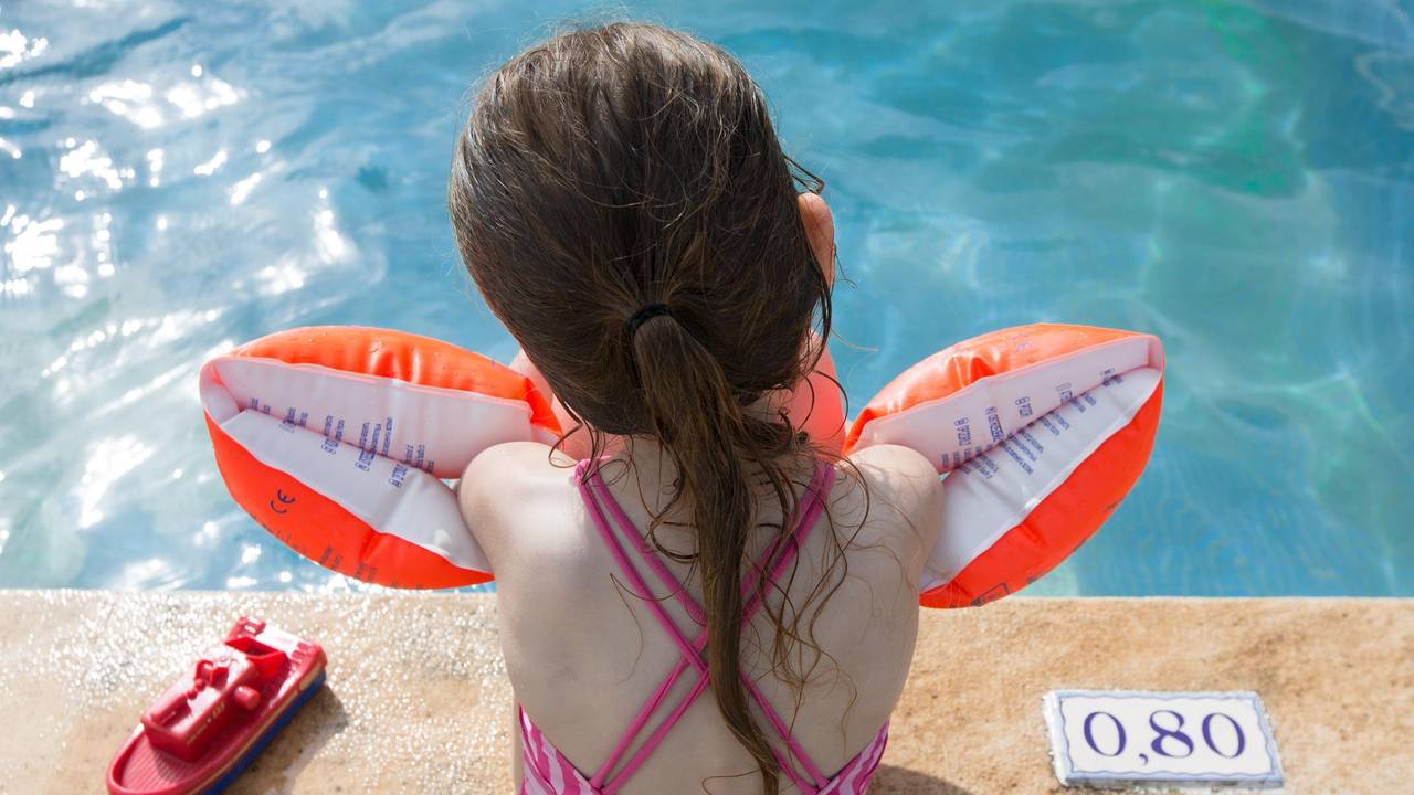 Ein Mädchen sitzt mit Schwimmflügeln am Beckenrand.