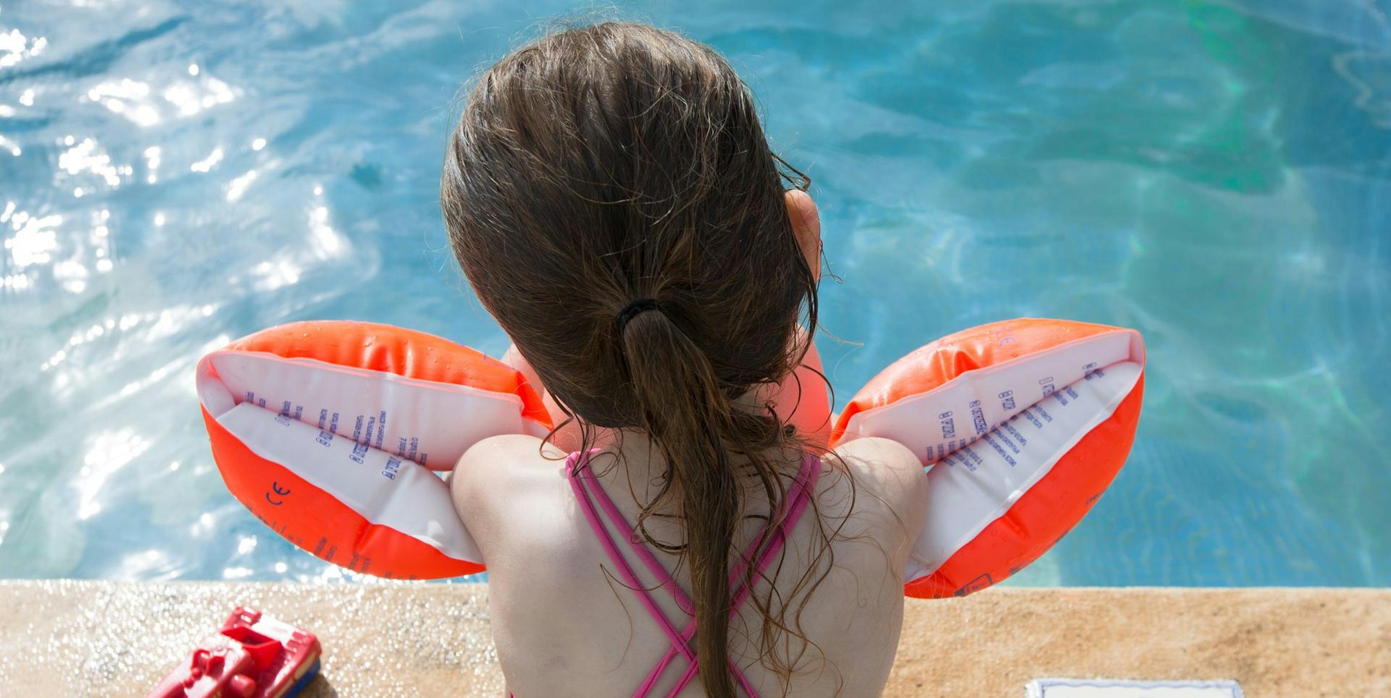 Ein Mädchen sitzt mit Schwimmflügeln am Beckenrand.