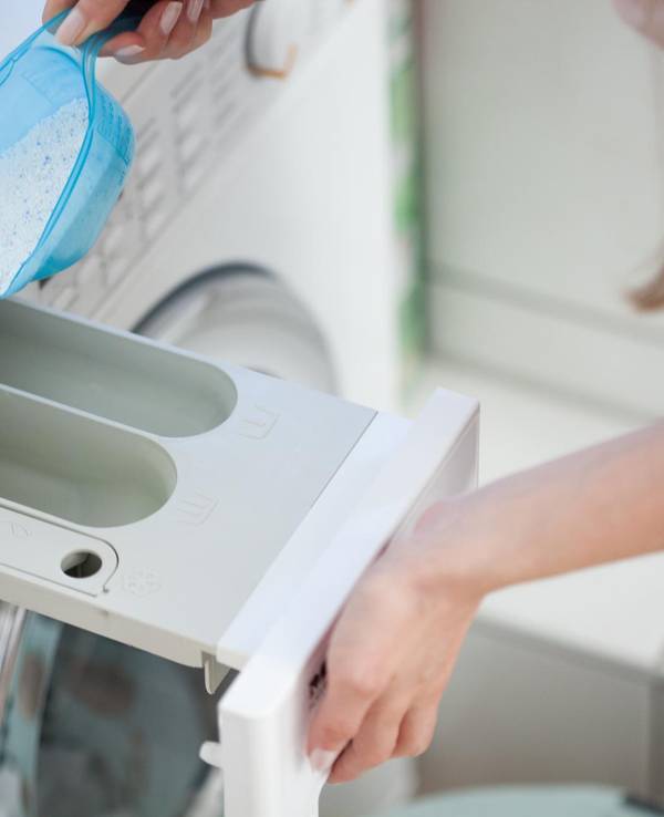 Frau füllt Waschmittel in eine Waschmaschine