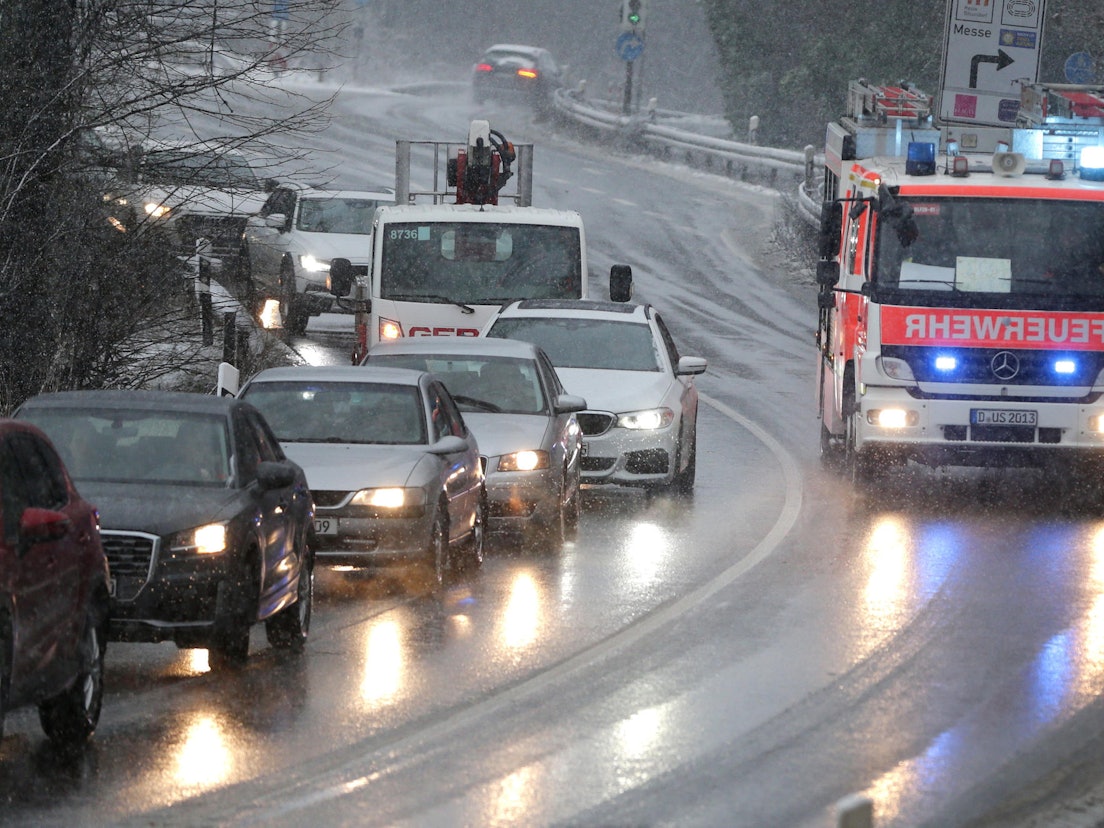 Ein Fahrzeug der Feuerwehr fährt mit Blaulicht bei Schneetreiben an einem Stau vorbei.