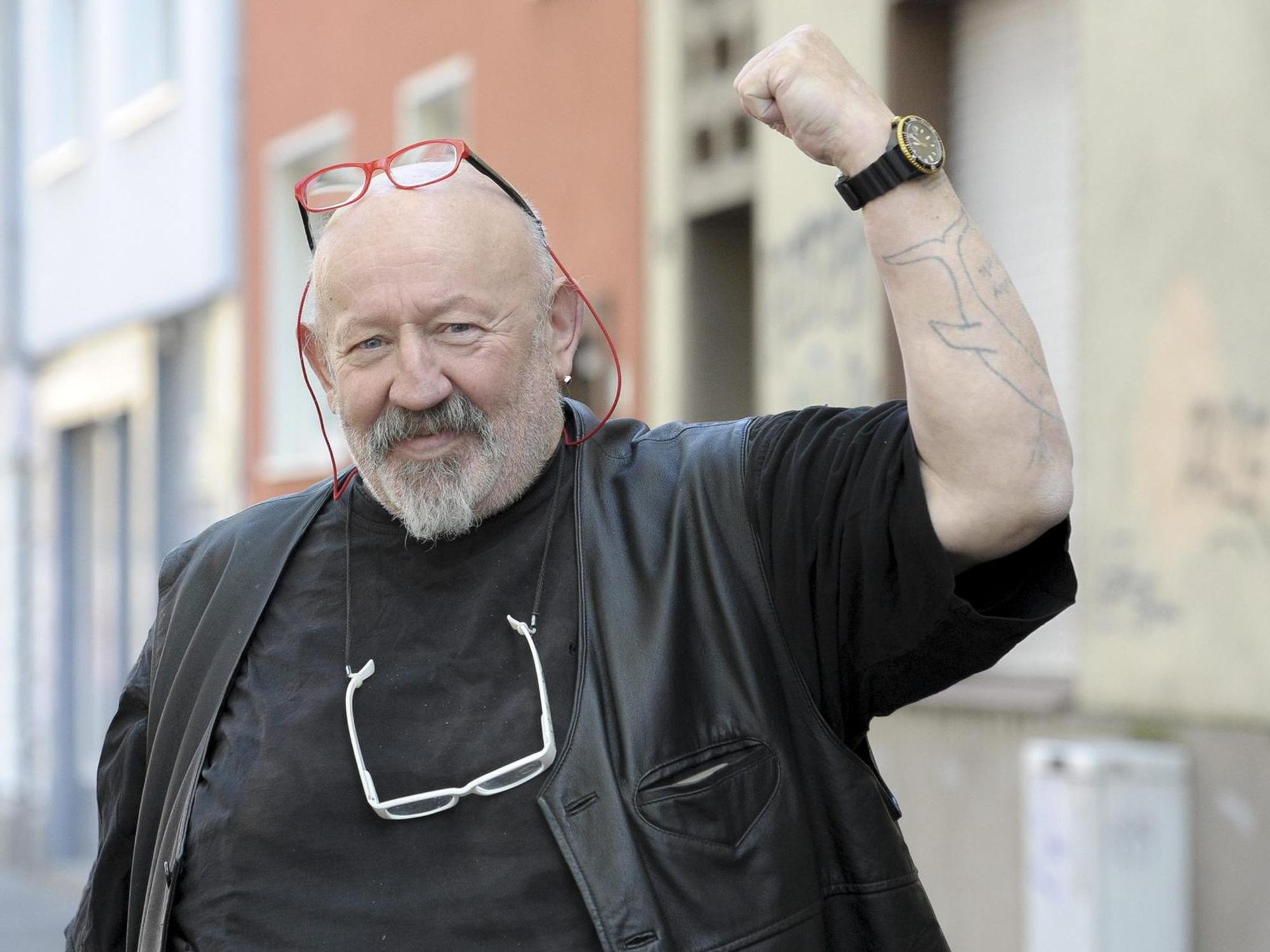 Jürgen Zeltinger reckt die Faust in die Höhe und lächelt in die Kamera.