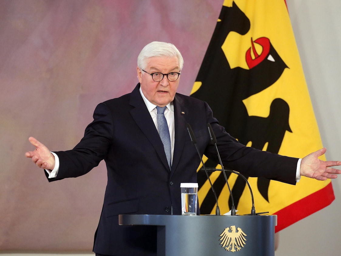 Das Symbolfoto von 2021 zeigt den deutschen Bundespräsidenten Frank-Walter Steinmeier. Er steht an einem Rednerpult mit drei Mikrofonen, hinter ihm befindet sich eine Flagge.