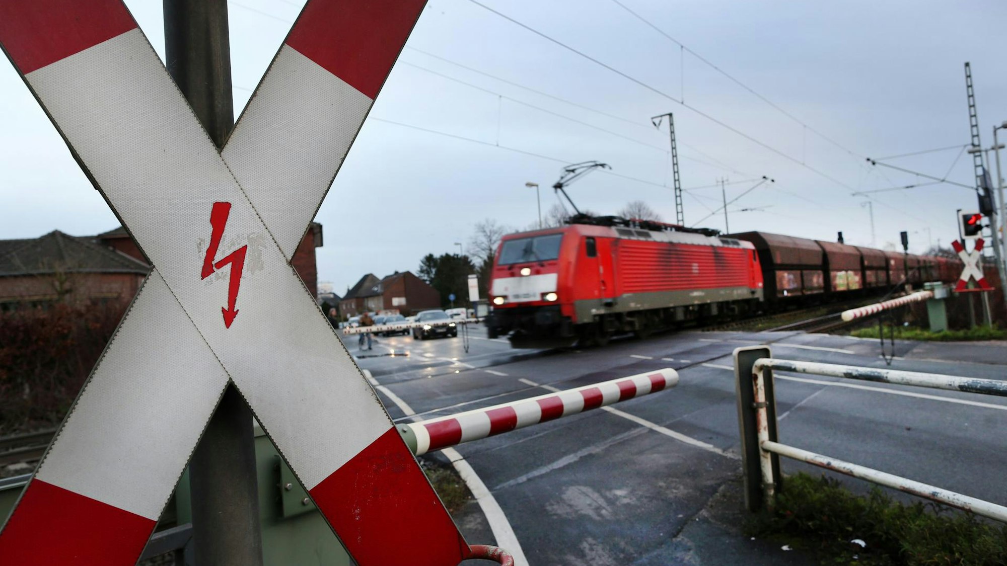 Ein Zug passiert einen Bahnübergang, vor den geschlossenen Halbschranken warten Autos.
