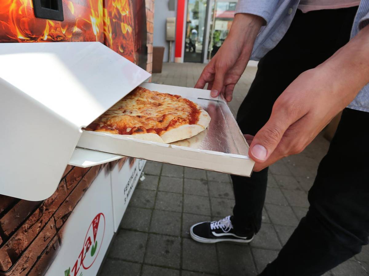 Ein Mann hält einen halbgeöffneten Pizzakarton in Händen.