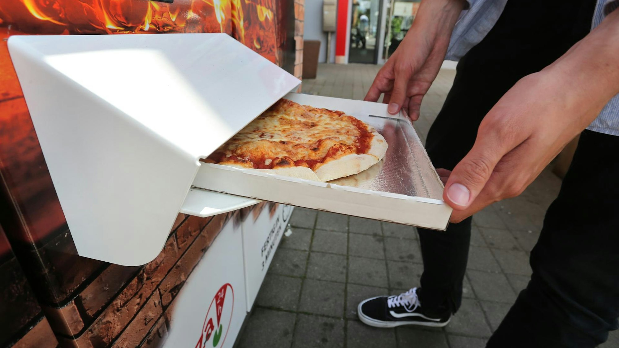 Ein Mann hält einen halbgeöffneten Pizzakarton in Händen.