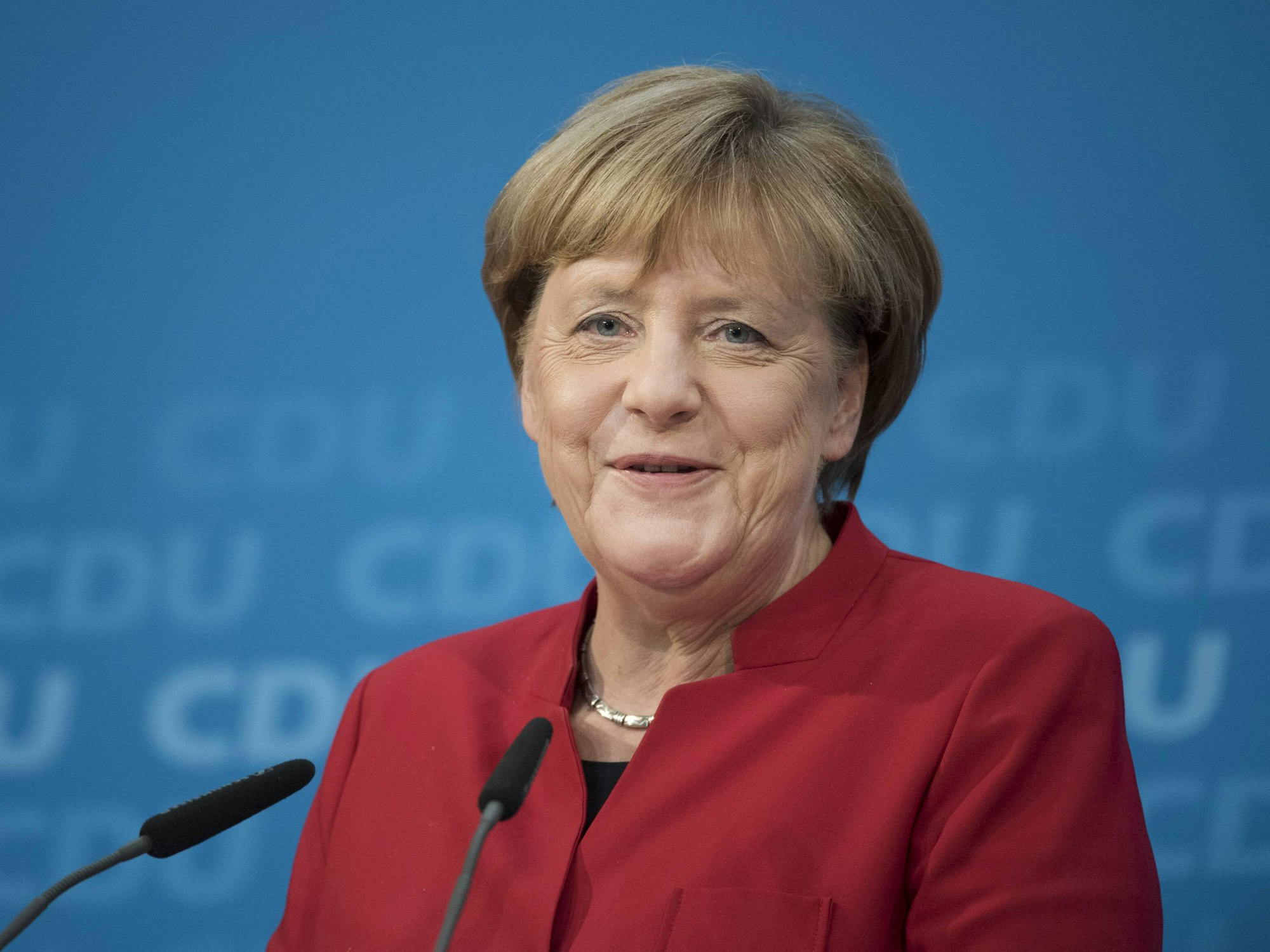 Angela Merkel grinst bei einem Pressestatement am Rednerpult.