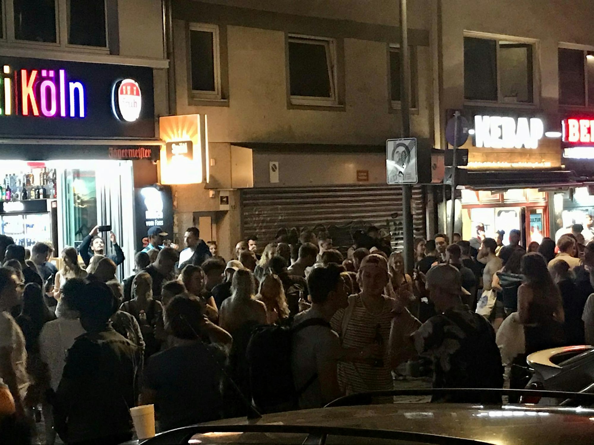 Viele Leute stehen dicht gedrängt vor einem Kiosk und anderen Lokalen an der Zülpicher Straße, Ecke Zülpicher Platz