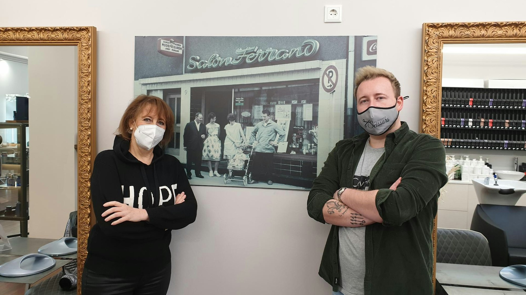 Die Kölner Friseure Annette (58) und Nils Ferrand (29) stehen vor einem alten Foto in ihrem Friseursalon.