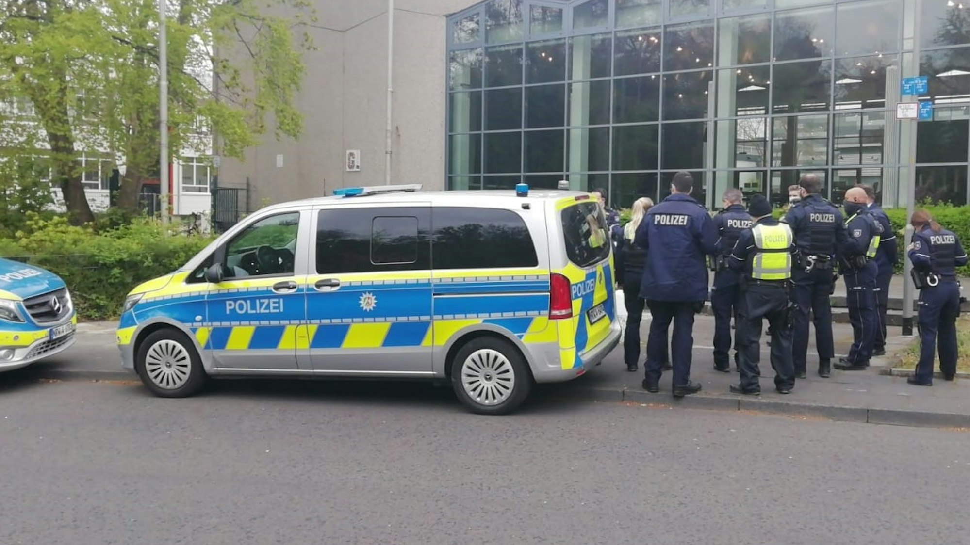 Polizeifahrzeuge und mehrere Einsatzkräfte stehen vor einem Gebäude.