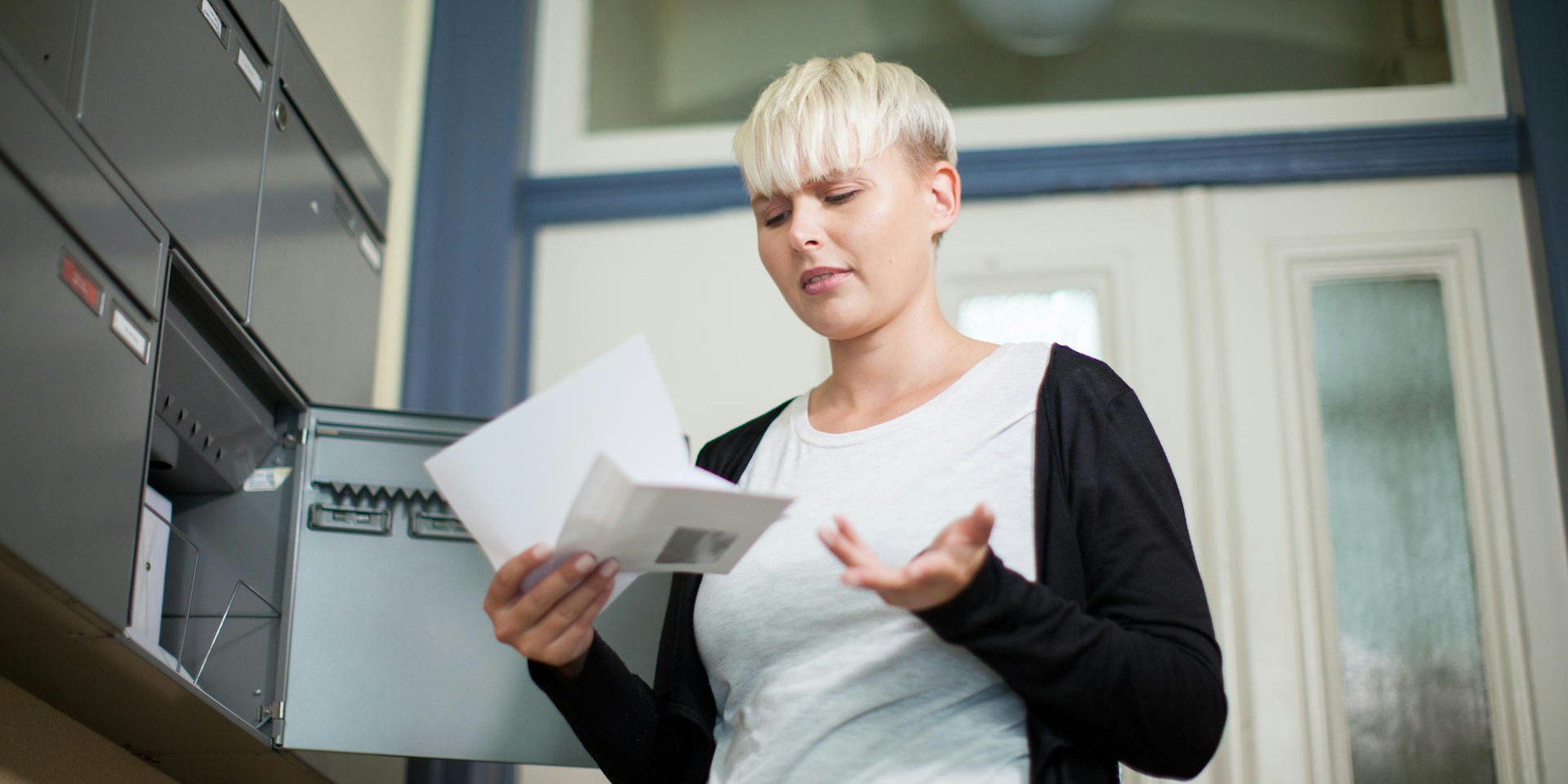 Frau_steht_am_Briefkasten_und ärgert_sich_über_Briefinhalt