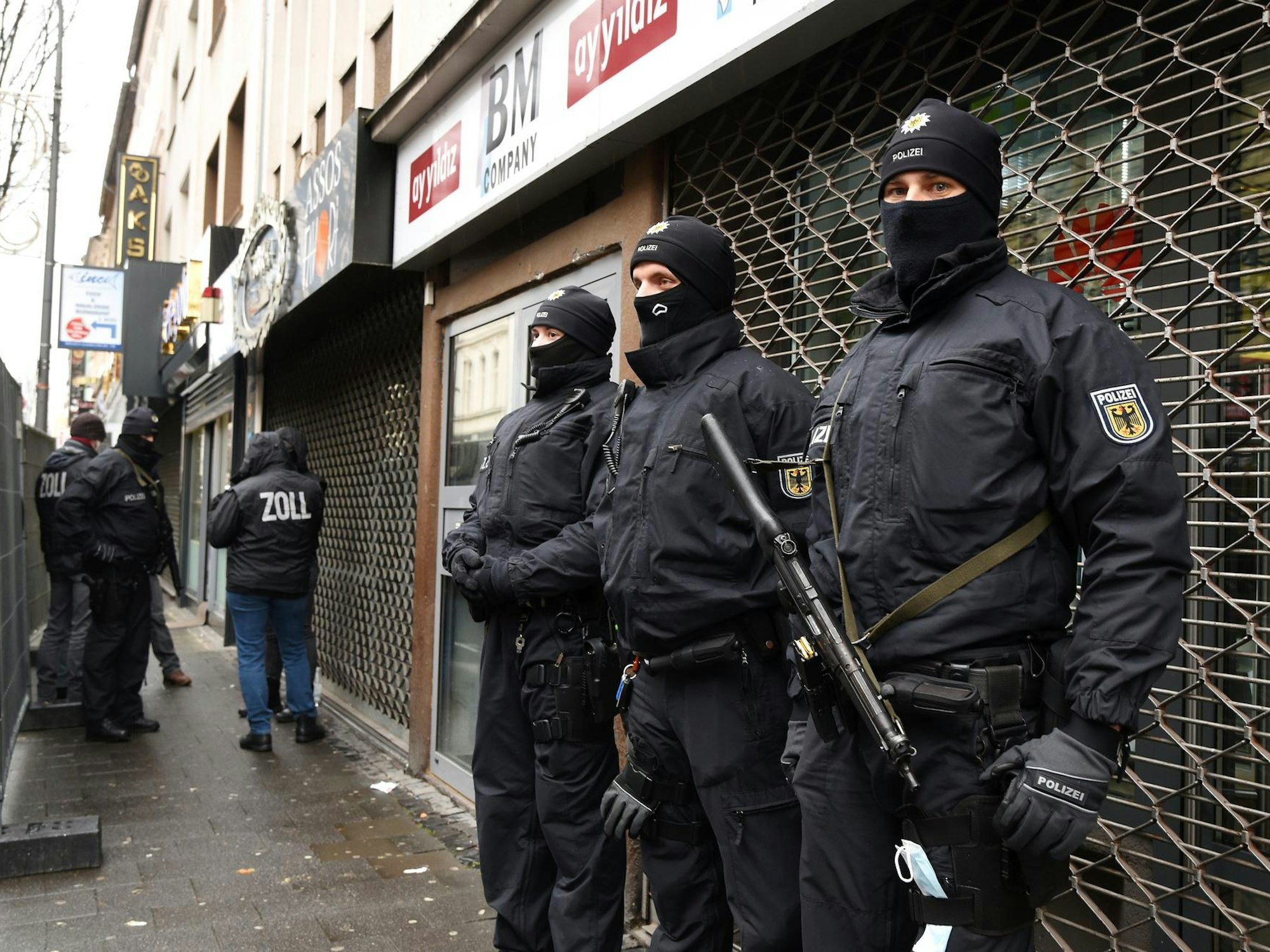 Schwer bewaffnete Einsatzkräfte stehen vor einem heruntergelassenen Rollgitter.