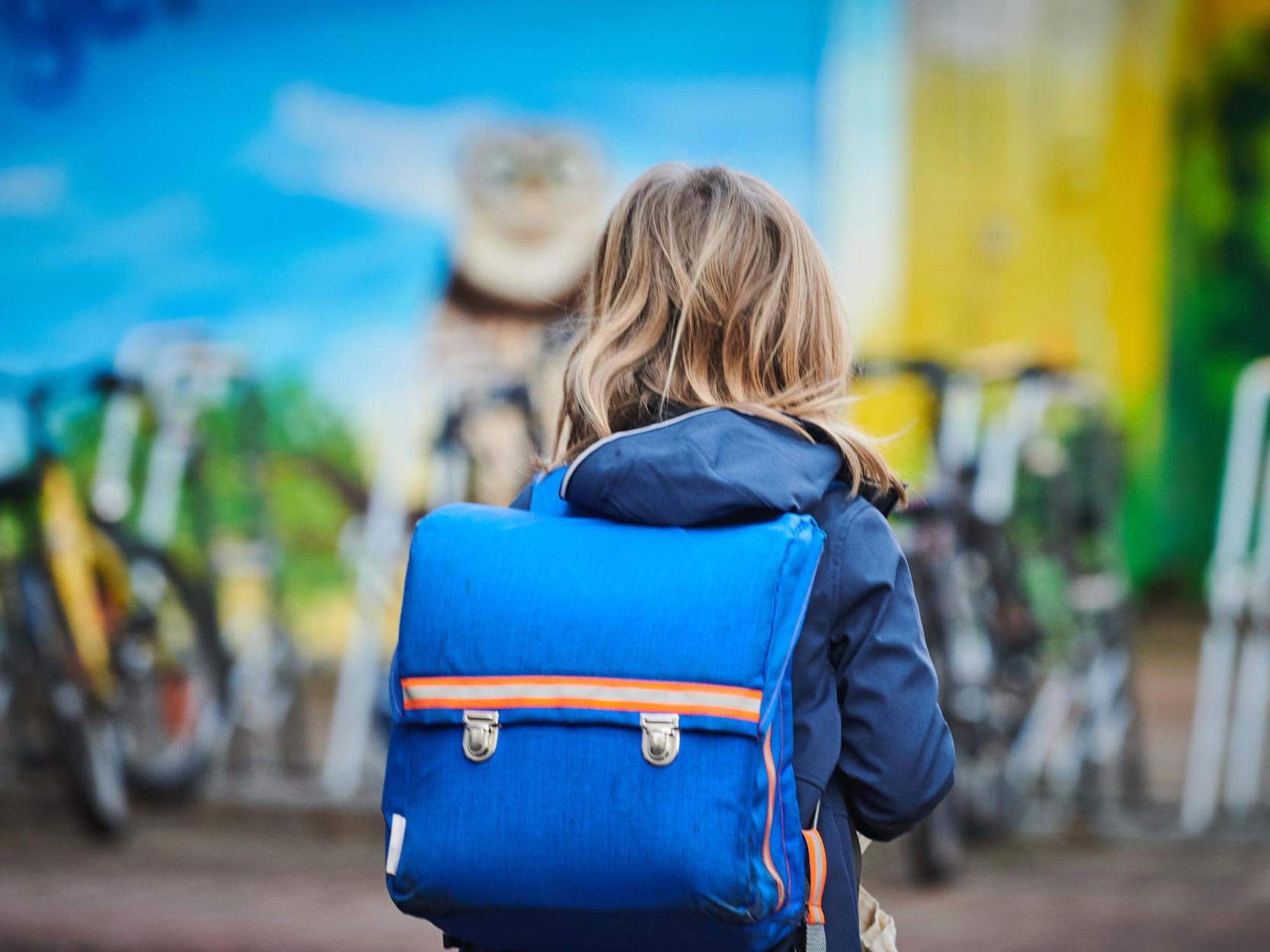 Eine Schülerin trägt einen Schulranzen auf dem Rücken.