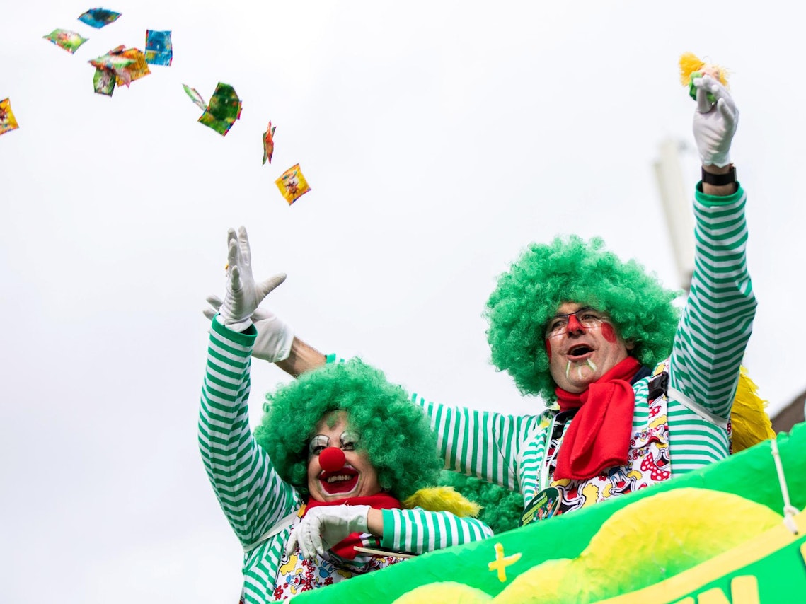 Zwei Jecke werfen Kamelle beim Rosenmontagszug vom Wagen