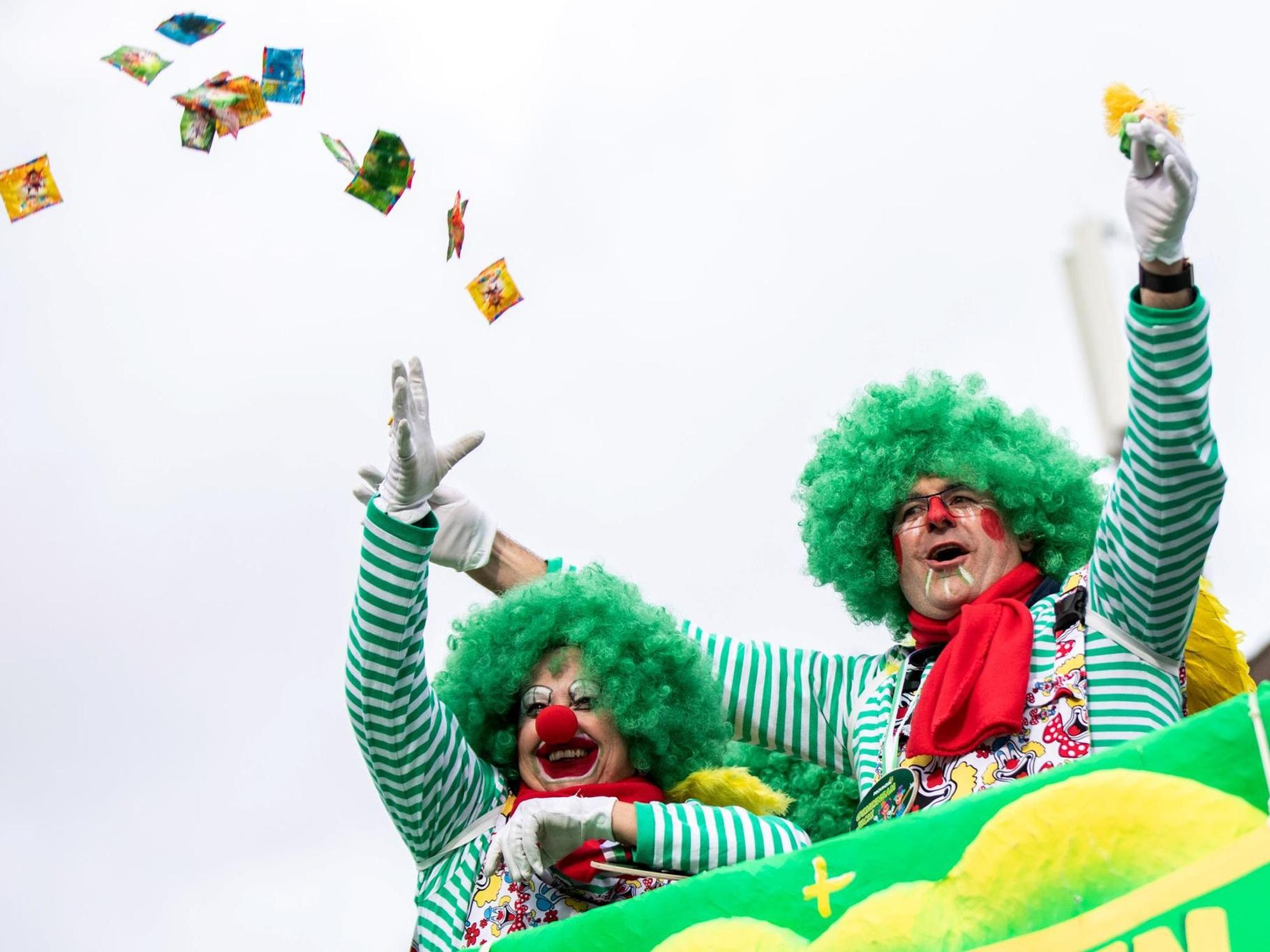 Zwei Jecke werfen Kamelle beim Rosenmontagszug vom Wagen