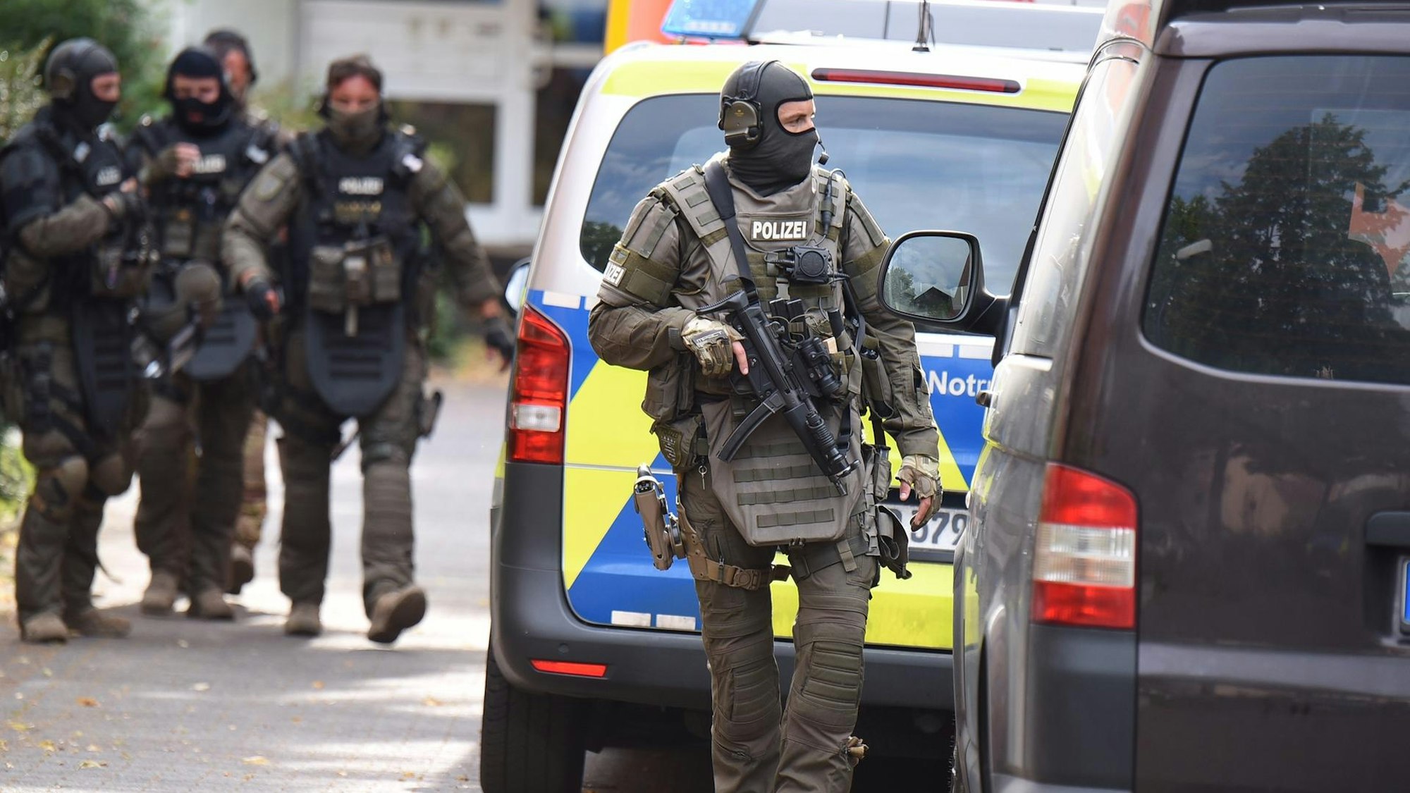 Bewaffnete Spezialkräfte bei einem Einsatz neben einem Polizeiwagen