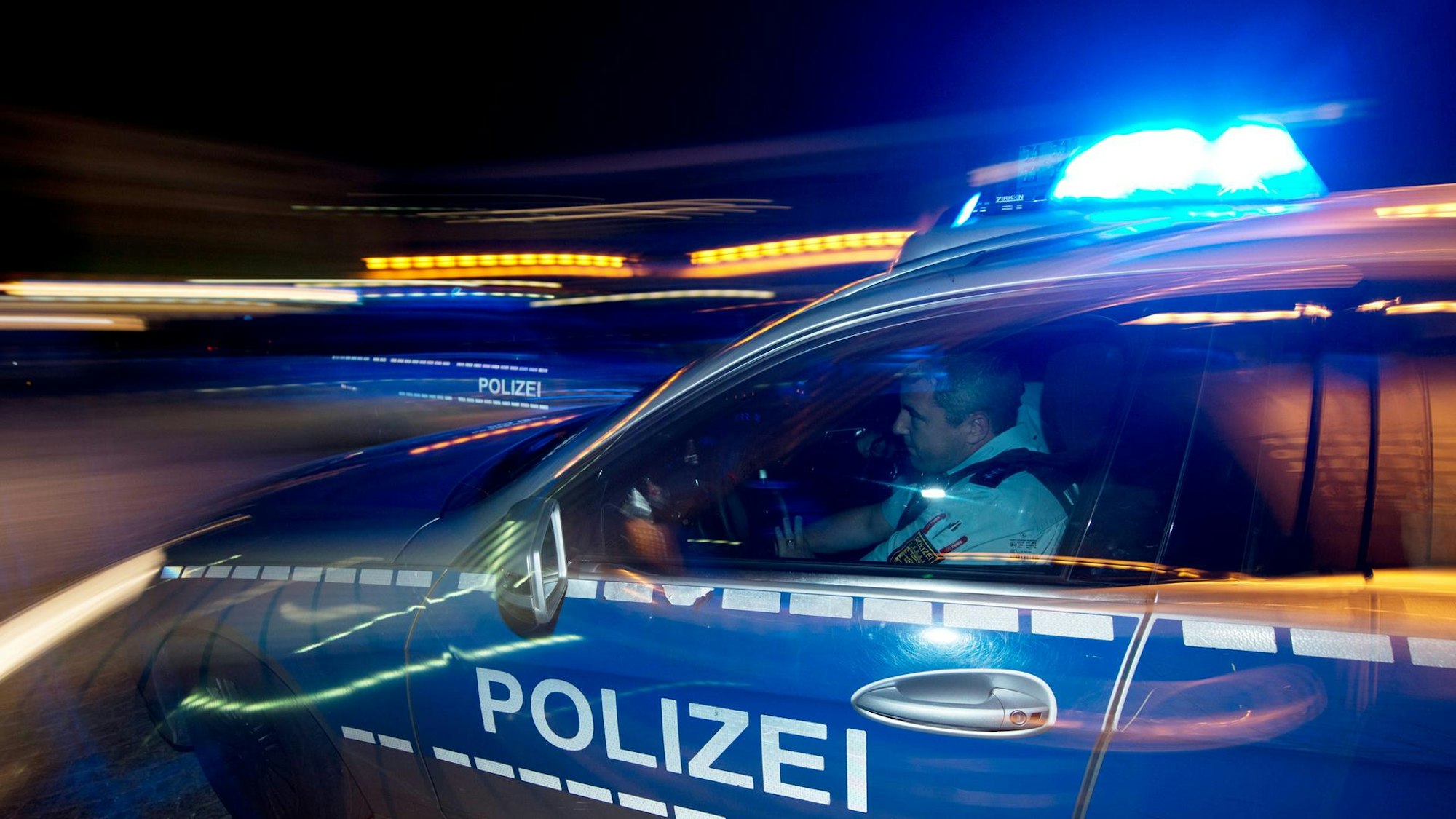 Ein Polizeiauto fährt nachts mit Blaulicht.