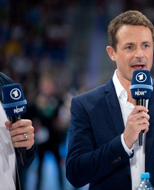 Alexander Bommes moderiert bei einer EM-Übertragung mit einem Mikrofon in der Hand..