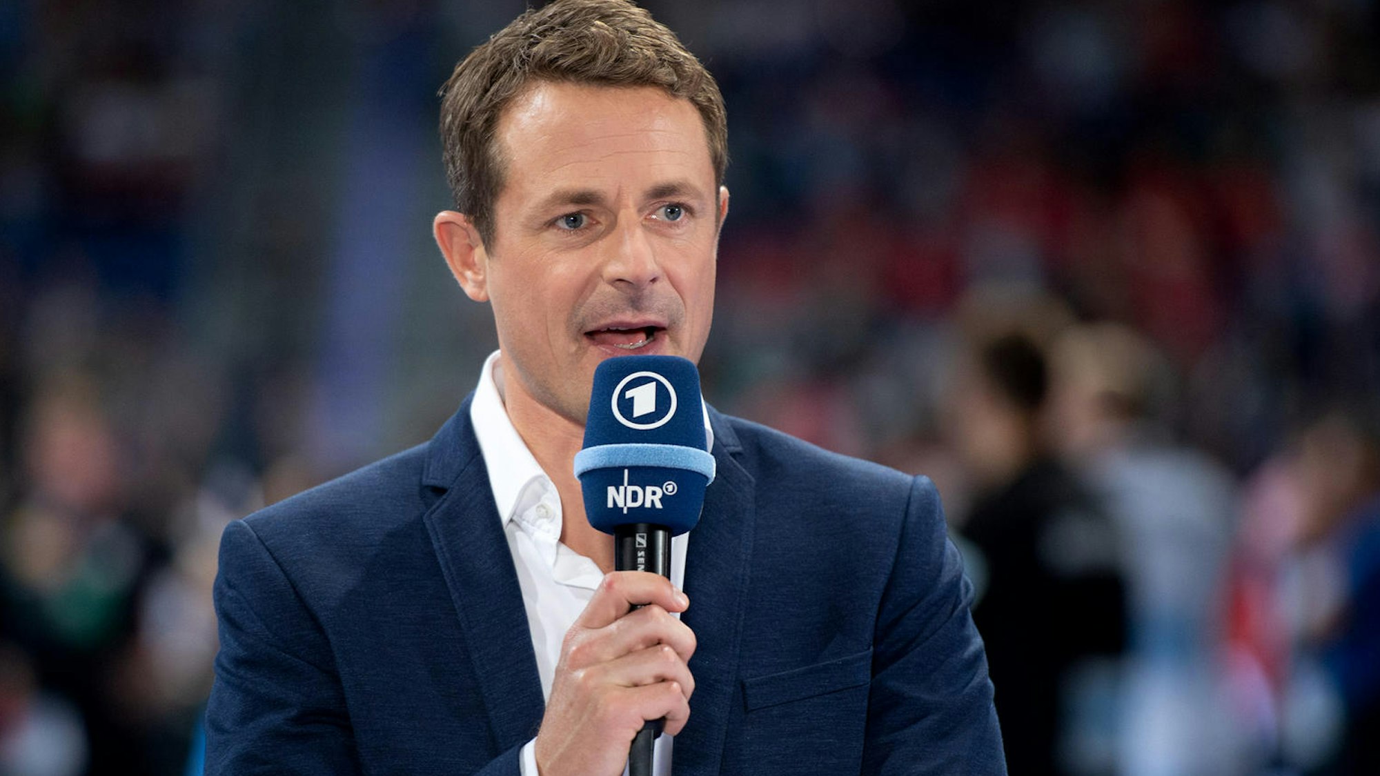 Alexander Bommes moderiert bei einer EM-Übertragung mit einem Mikrofon in der Hand..