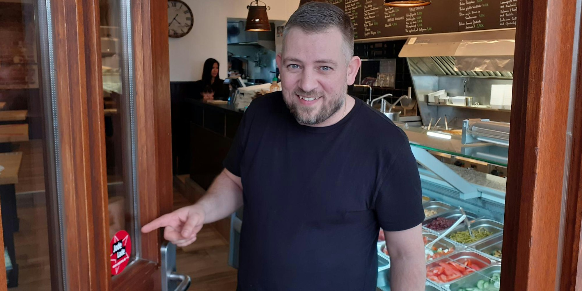 Christos Charalabidis zeigt den Jode-Lade-Sticker an seinem Laden Tischlein deck dich.