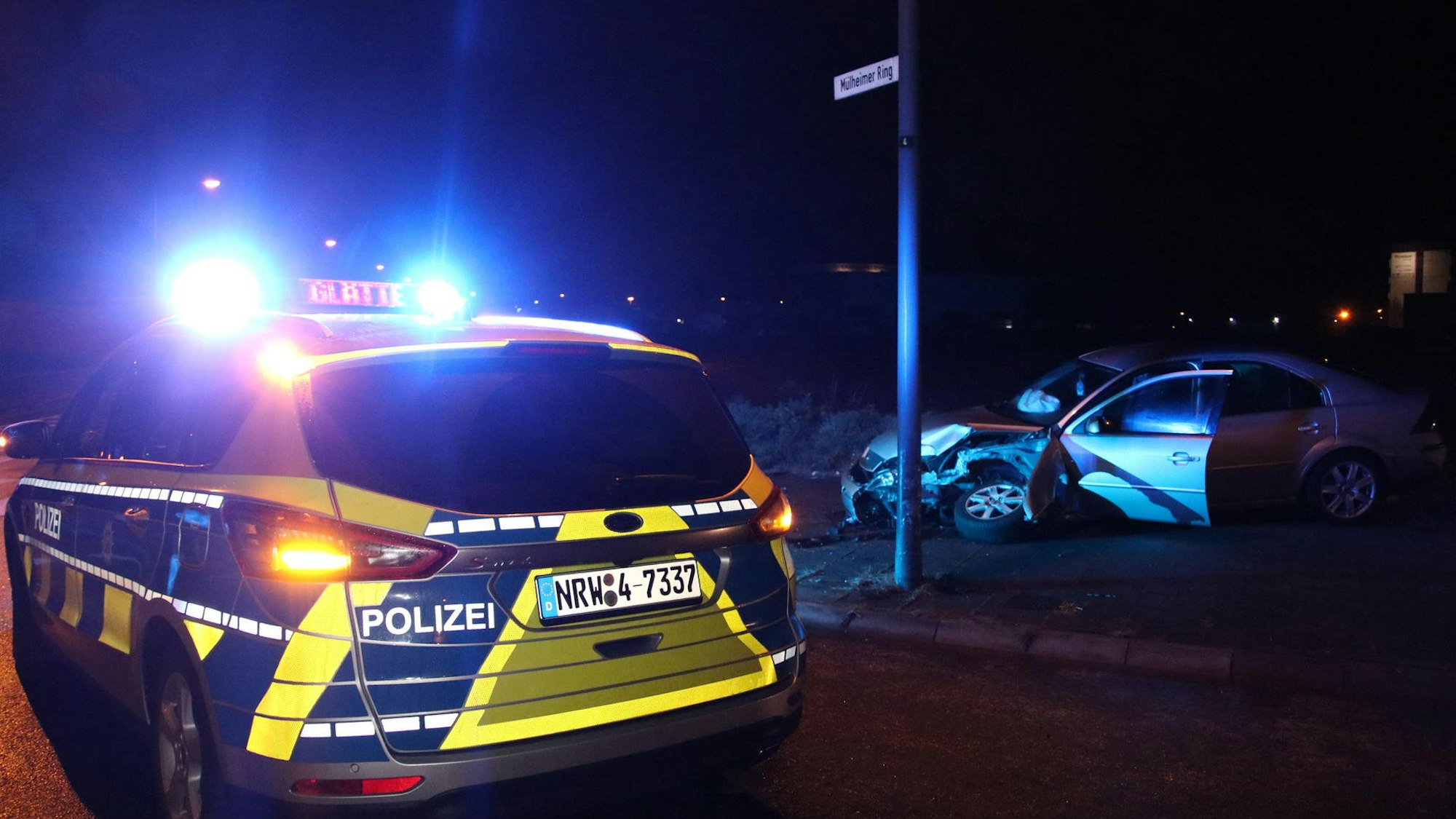 Ein Polizeifahrzeug steht neben einem völlig beschädigten Auto.