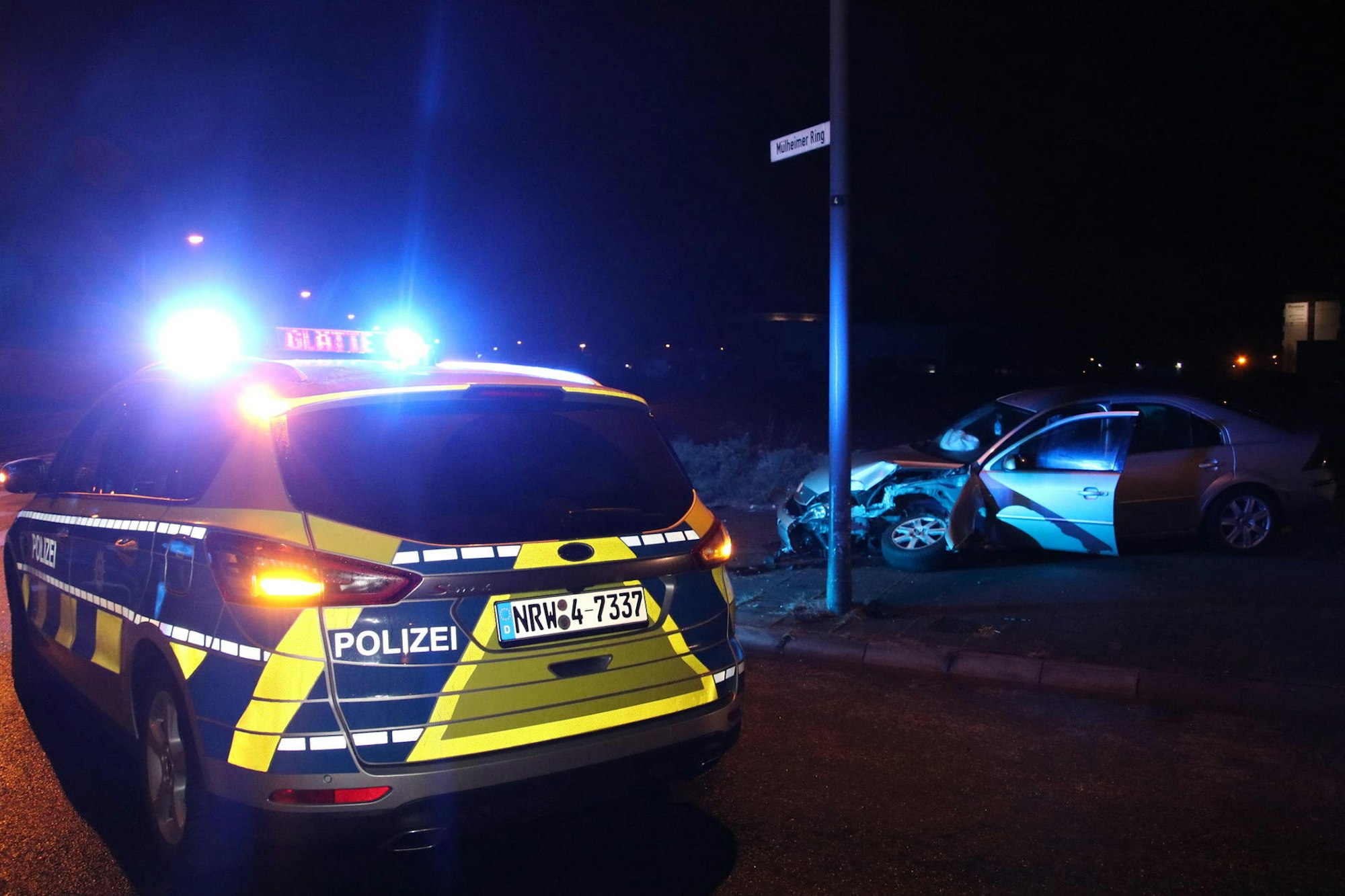 Ein Polizeiwagen steht in Köln-Mülheim neben einem verunfallten Pkw.