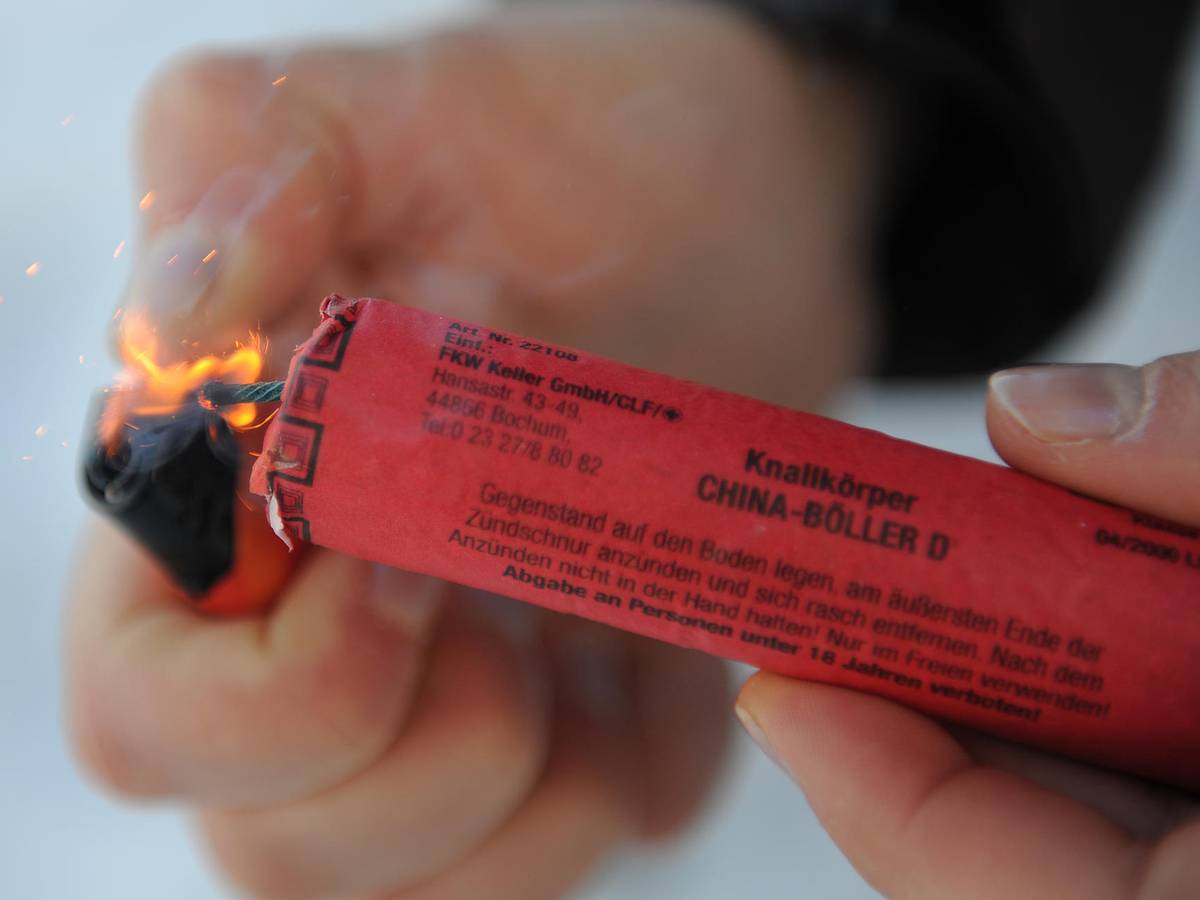 Das Symbolfoto zeigt einen roten Feuerwerkskörper, der mit einem Feuerzeug angezündet wird.