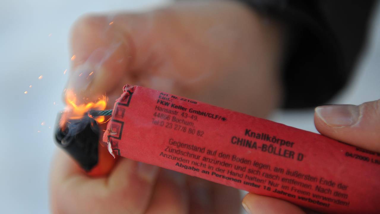 Das Symbolfoto zeigt einen roten Feuerwerkskörper, der mit einem Feuerzeug angezündet wird.