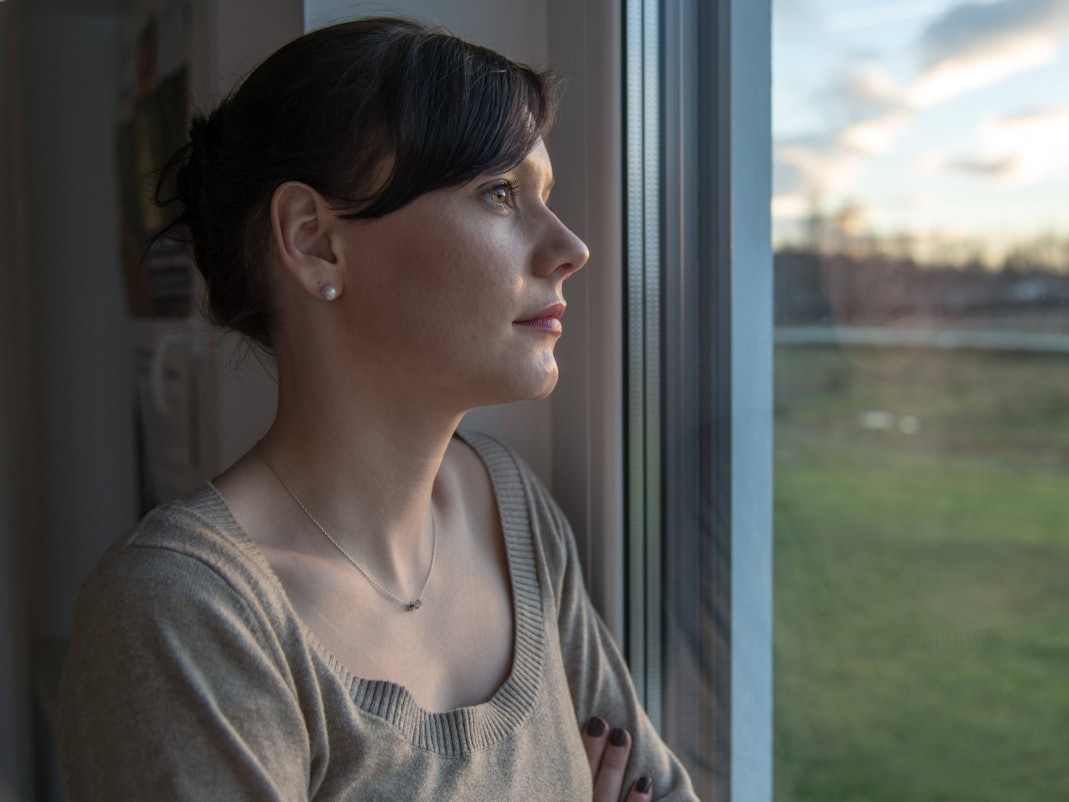 Eine Frau schaut nachdenklich aus dem Fenster.